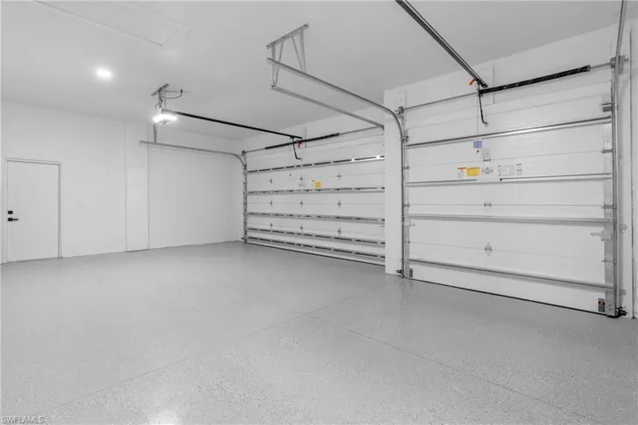 Spacious three-car garage featuring a light gray epoxy floor coating, white walls, and two overhead garage doors