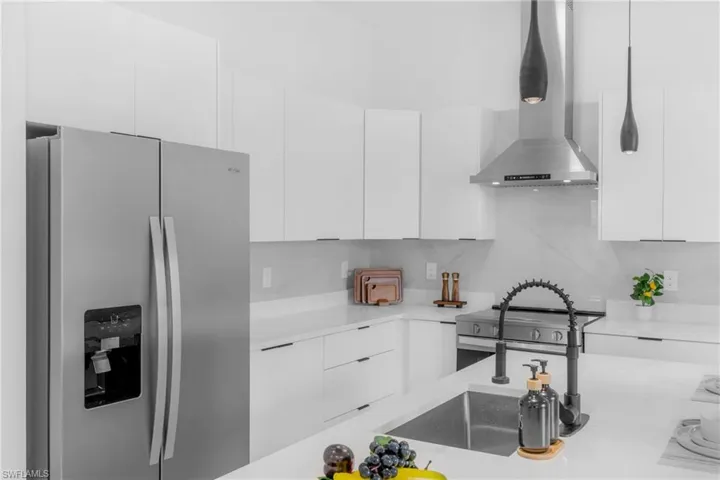 Modern kitchen featuring white cabinetry, stainless steel appliances, a large sink with a flexible black faucet, white countertops, and contemporary pendant lighting
