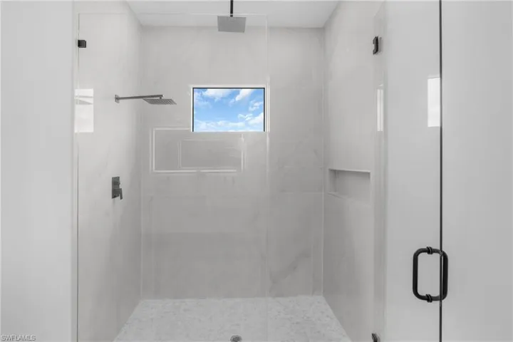 Glass-enclosed shower featuring large format tile walls, a window, and two recessed niches