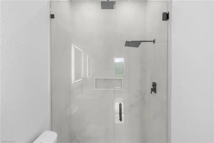 Glass-enclosed shower featuring dual matte black rain shower heads, a built-in recessed niche, and large format wall tiling