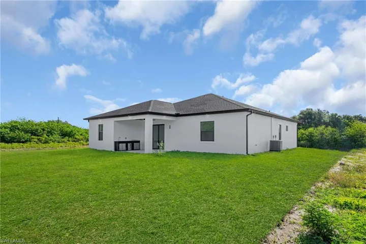 Expansive green lawn surrounds the rear of the property, featuring a white stucco exterior and dark-framed windows
