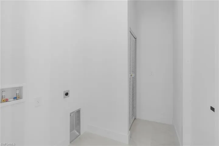 Dedicated laundry area featuring a louvered door, white walls, and light-toned flooring