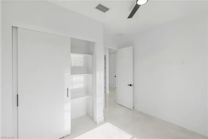 Bright room featuring a large sliding door closet with interior shelving, polished tile flooring, and a modern ceiling fan with integrated lighting