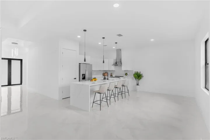 Modern kitchen featuring an extended island with waterfall-edge countertop, stainless steel appliances, recessed lighting, and pendant light fixtures