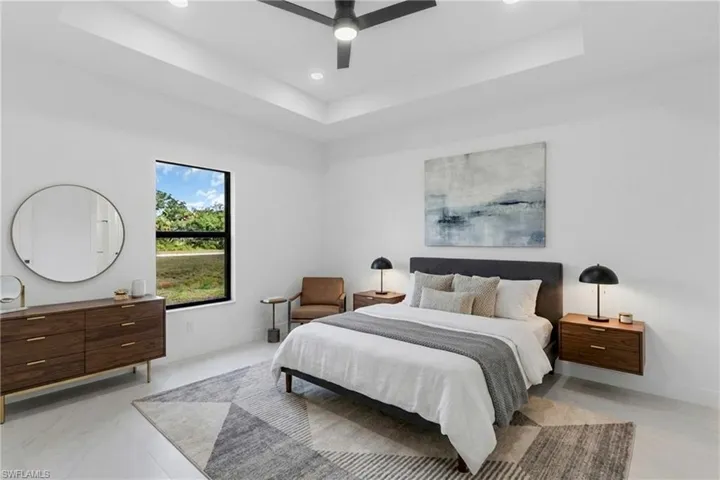 Virtually Staged.  Spacious room featuring a tray ceiling with recessed lighting and a ceiling fan, a large window, light-toned flooring, and white walls