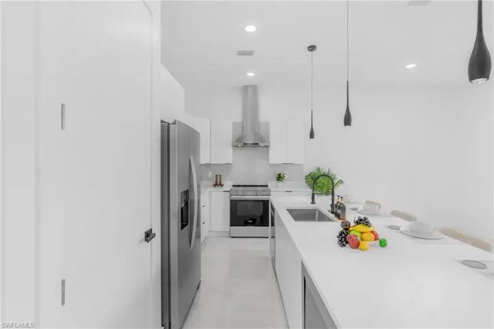 Modern kitchen featuring a large island with an undermount sink and matte black faucet, stainless steel appliances, white cabinetry, a tiled backsplash, and recessed and pendant lighting