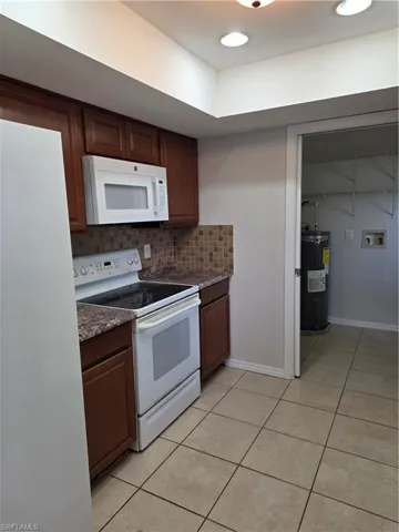 Kitchen featuring white appliances, decorative backsplash, light tile patterned flooring, dark wood finish cabinets, and recessed lighting
