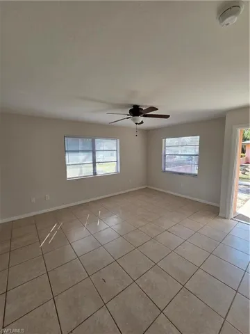 Empty room with a ceiling fan, light tile patterned floors, and a smoke detector