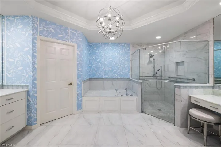 Full bathroom featuring a garden tub, a tray ceiling, vanity, a marble finish shower, and ornamental molding