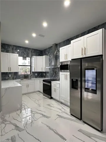 Kitchen with stainless steel appliances, light stone countertops, recessed lighting, white cabinets, and light marble finish flooring