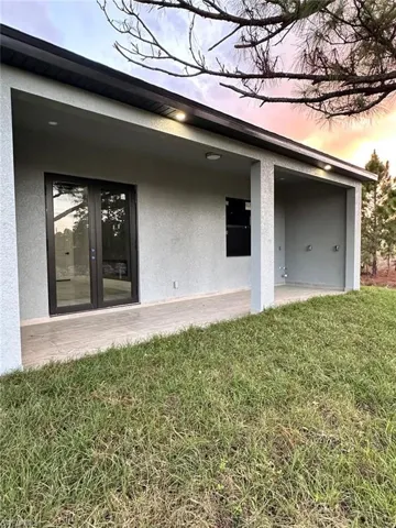 Exterior entry at dusk featuring a yard, stucco siding, french doors, and a patio