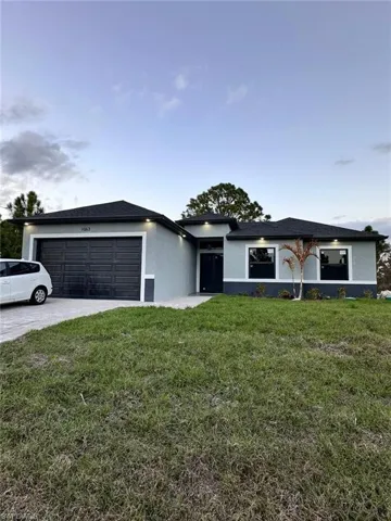 View of front of house with stucco siding, a front lawn, an attached garage, and concrete driveway