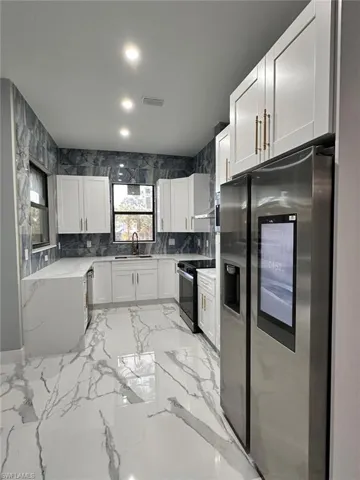 Kitchen featuring stainless steel appliances, white cabinets, light stone counters, recessed lighting, and light marble finish flooring