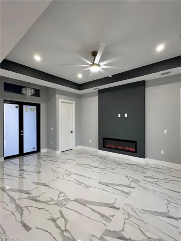 Unfurnished living room featuring recessed lighting, a ceiling fan, a tray ceiling, a large fireplace, and french doors