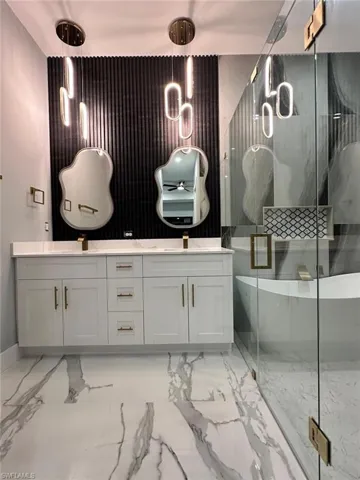 Bathroom with double vanity, light marble finish floors, and a marble finish shower