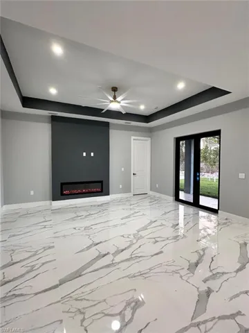 Unfurnished living room with a raised ceiling, a ceiling fan, recessed lighting, french doors, and a fireplace