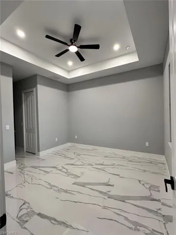 Unfurnished room featuring recessed lighting, a tray ceiling, a ceiling fan, and light marble finish floors