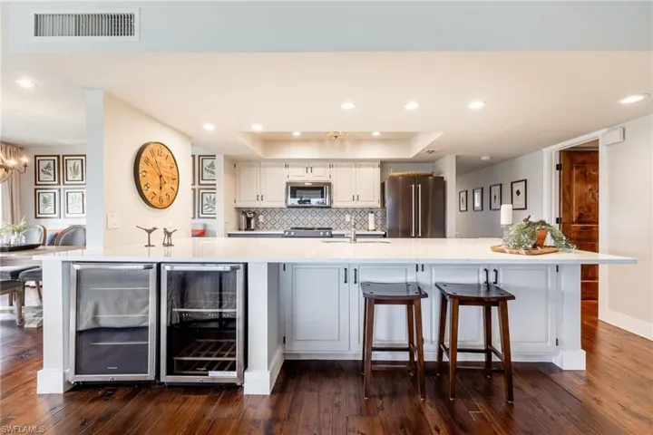 Kitchen featuring wine cooler, beverage fridge a large island with sink, stainless steel appliances, and dark hardwood  floors