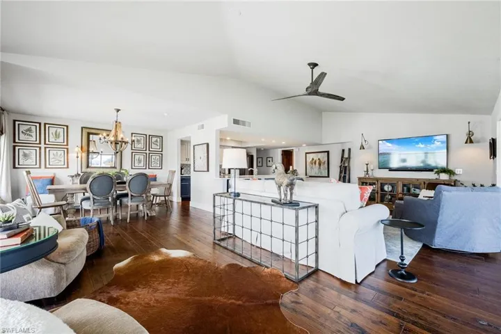 Living room with lofted ceiling, dark wood-type flooring, and ceiling fan with notable chandelier