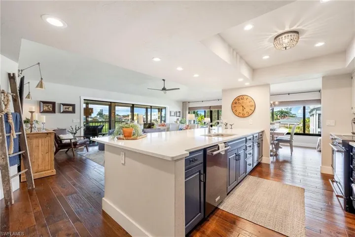 Kitchen with appliances with stainless steel finishes, light stone countertops, dark wood-type flooring, ceiling fan with notable chandelier, and sink
