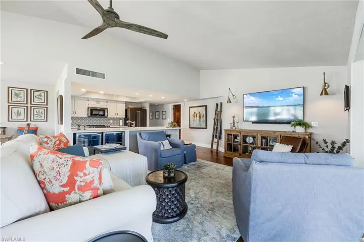 Living room with wine cooler, ceiling fan, wood-type flooring, and vaulted ceiling