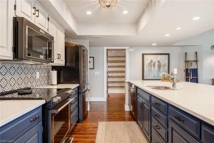 Kitchen featuring white & blue cabinetry, stainless steel appliances, sink, and hardwood flooring