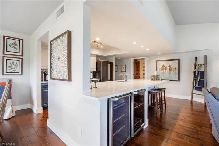 Kitchen with wine cooler, high quality fridge, dark wood-type flooring, and a kitchen bar