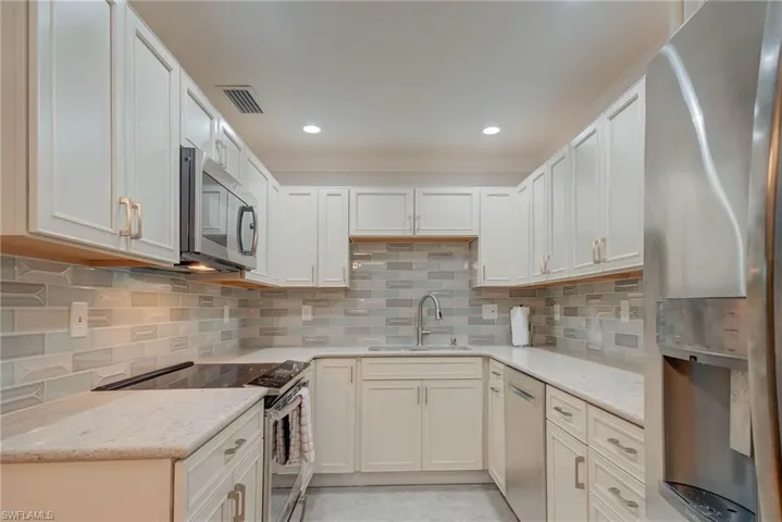 Kitchen with appliances with stainless steel finishes, backsplash, light stone countertops, recessed lighting, and white cabinetry