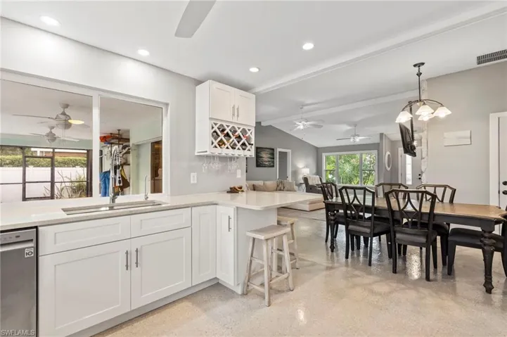Kitchen featuring decorative light fixtures, lofted ceiling with beams, white cabinetry, stainless steel dishwasher, and kitchen peninsula