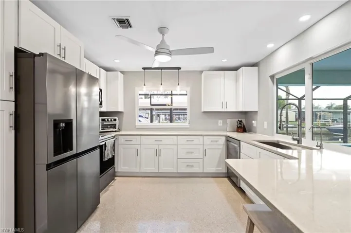 Kitchen featuring sink, light stone counters, ceiling fan, stainless steel appliances, and white cabinets