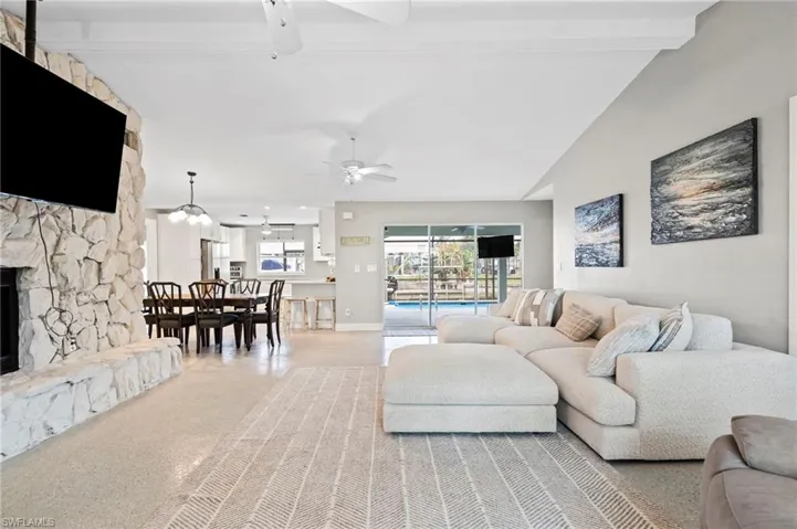 Living room with beamed ceiling, ceiling fan, a stone fireplace, and high vaulted ceiling