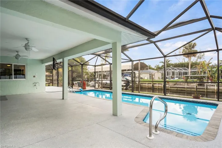 View of swimming pool featuring a lanai, a patio area, ceiling fan, and a water view