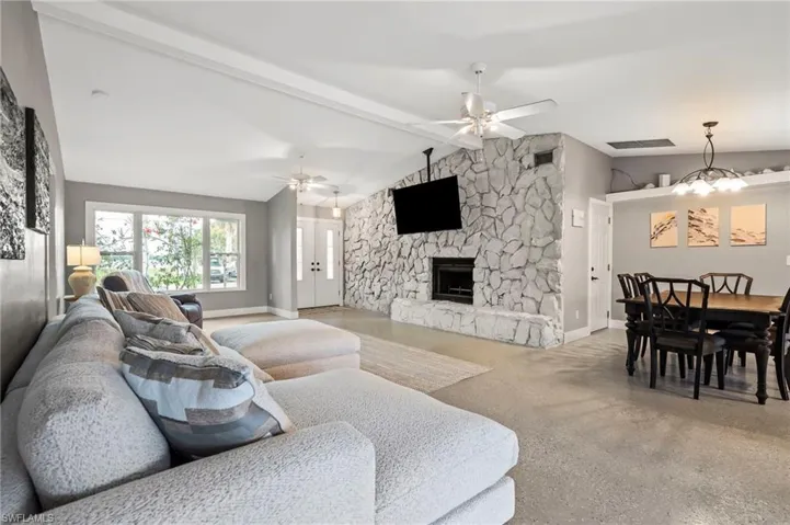 Living room featuring ceiling fan with notable chandelier, a fireplace, and lofted ceiling with beams