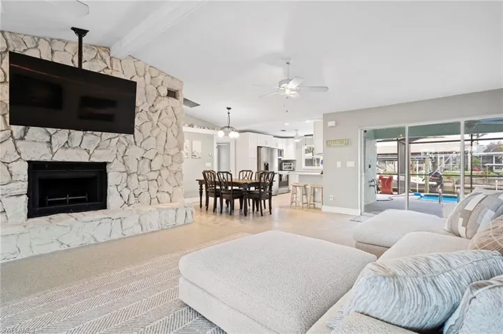Living room with ceiling fan, a fireplace, and lofted ceiling with beams