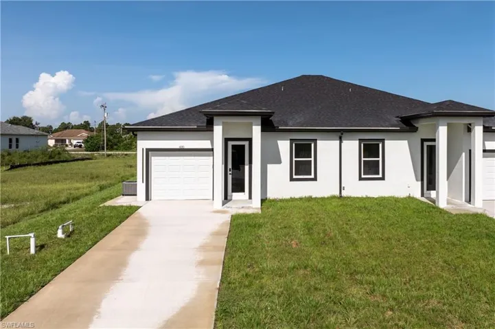 View of front of house with stucco siding, concrete driveway, a garage, roof with shingles, and a front yard