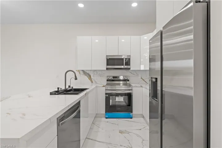 Kitchen with modern cabinets, stainless steel appliances, white cabinetry, light marble finish floors, and a peninsula
