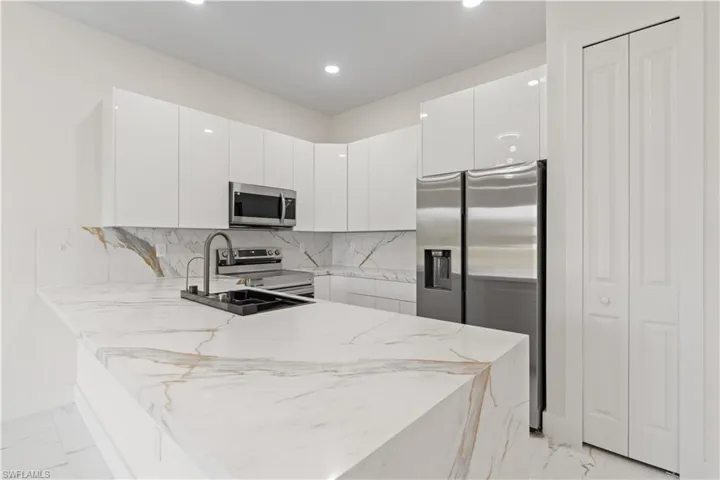 Kitchen featuring light marble finish floors, backsplash, stainless steel appliances, modern cabinets, and a peninsula