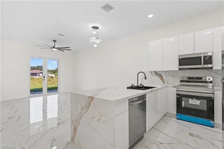 Kitchen with a peninsula, stainless steel appliances, light marble finish floors, modern cabinets, and white cabinetry