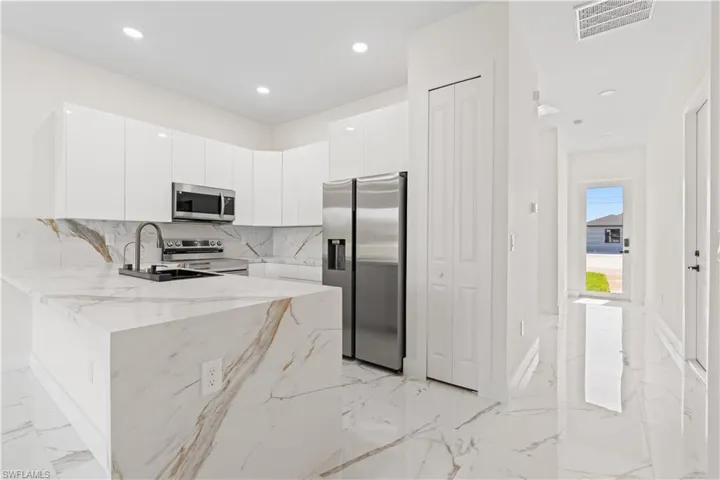 Kitchen with decorative backsplash, a peninsula, stainless steel appliances, light marble finish flooring, and light stone countertops