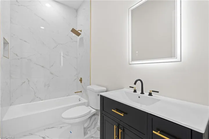 Full bath featuring vanity, marble look tiles, and shower / tub combination