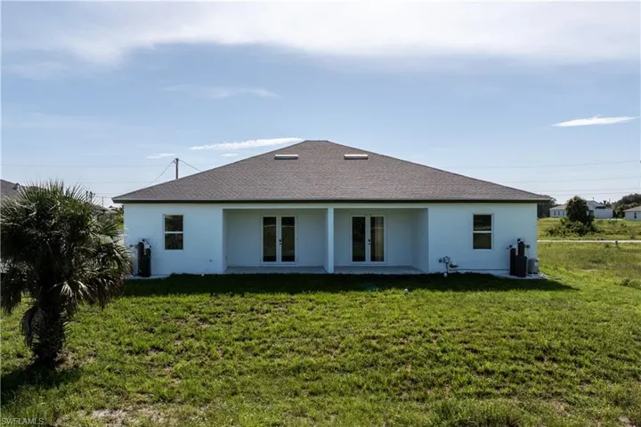Rear view of house with stucco siding, french doors, a lawn, and roof with shingles