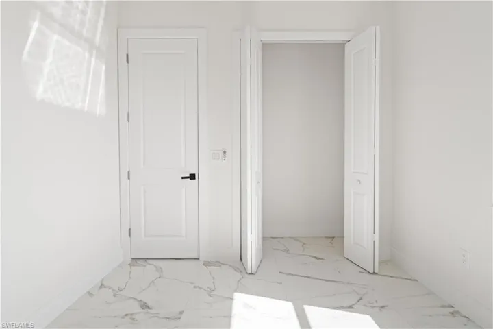 Unfurnished bedroom featuring marble look tiles and baseboards