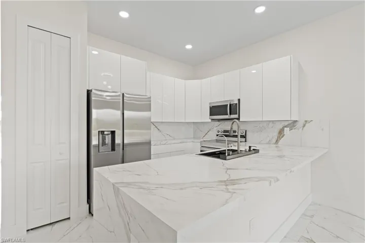 Kitchen featuring light marble finish floors, a peninsula, modern cabinets, white cabinets, and recessed lighting