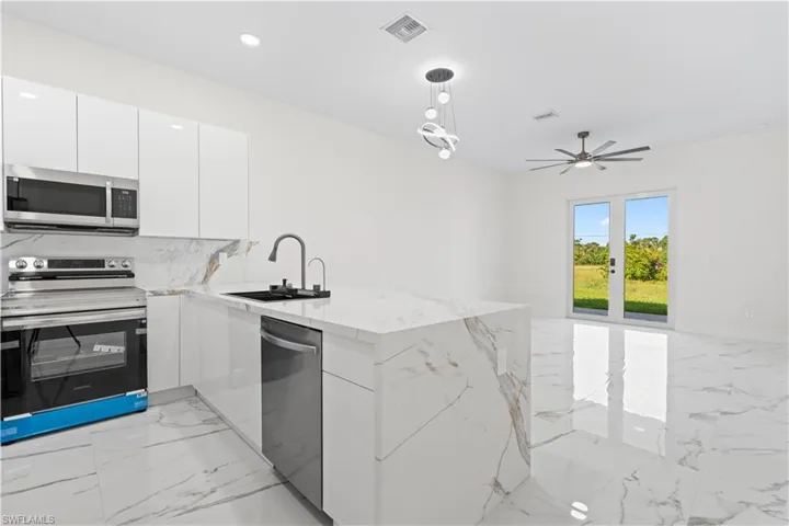 Kitchen with light marble finish flooring, appliances with stainless steel finishes, a peninsula, modern cabinets, and white cabinets