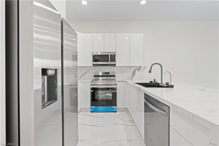 Kitchen featuring modern cabinets, stainless steel appliances, white cabinets, recessed lighting, and decorative backsplash