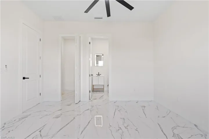 Unfurnished bedroom featuring light marble finish floors, ensuite bath, and ceiling fan