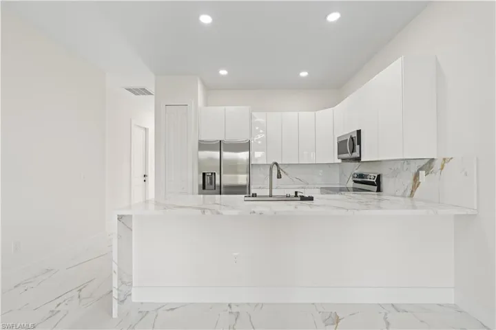 Kitchen with light stone counters, light marble finish floors, a peninsula, appliances with stainless steel finishes, and decorative backsplash