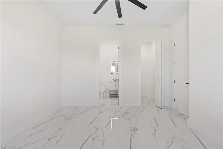 Unfurnished bedroom featuring marble look tiles, ensuite bathroom, and a ceiling fan