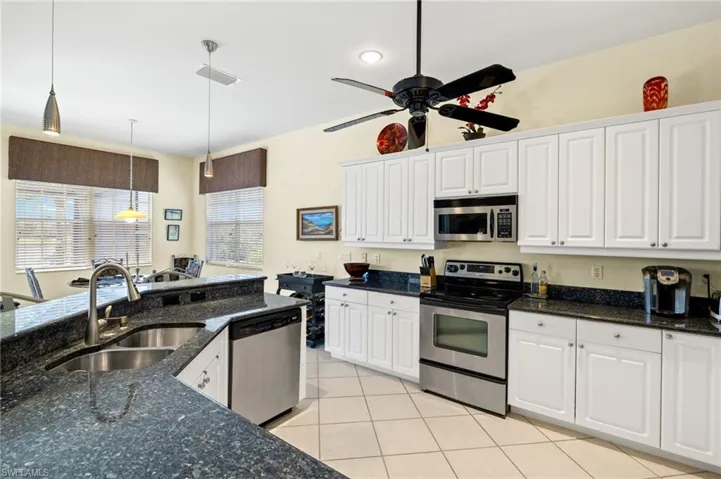 Kitchen featuring a sink, light tile patterned flooring, pendant lighting, stainless steel appliances, and white cabinets