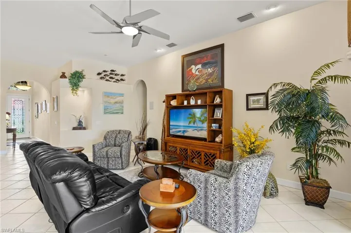 Living room featuring a ceiling fan, visible vents, arched walkways, and light tile patterned floors